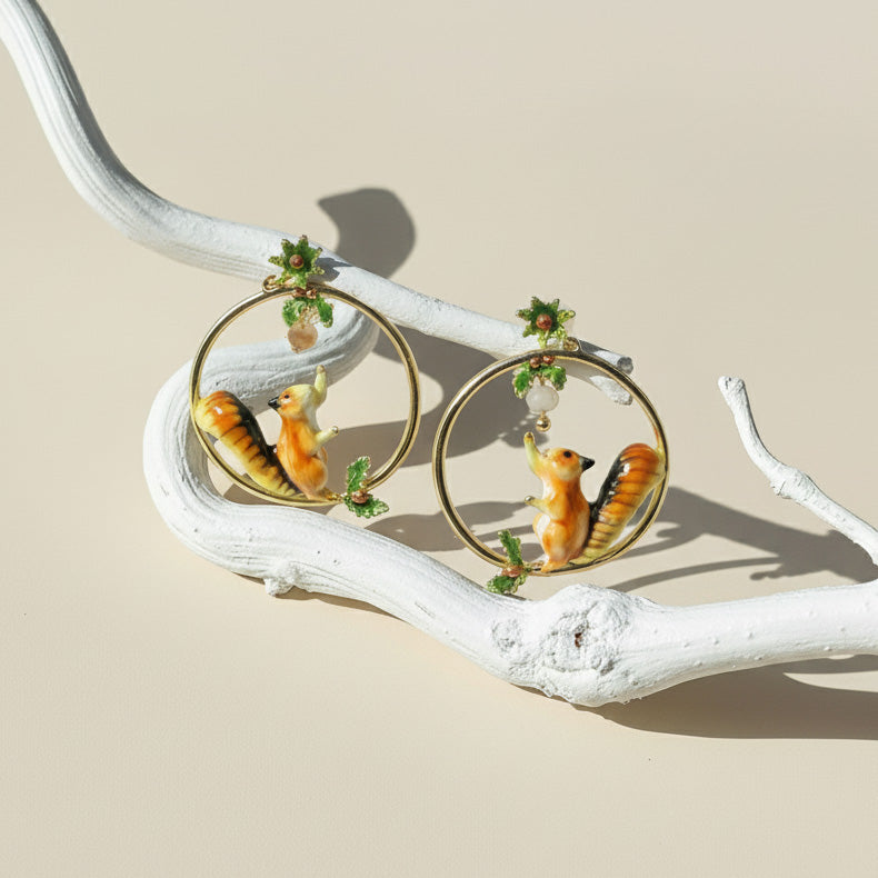 Earrings with animal designs on a branch against a beige background