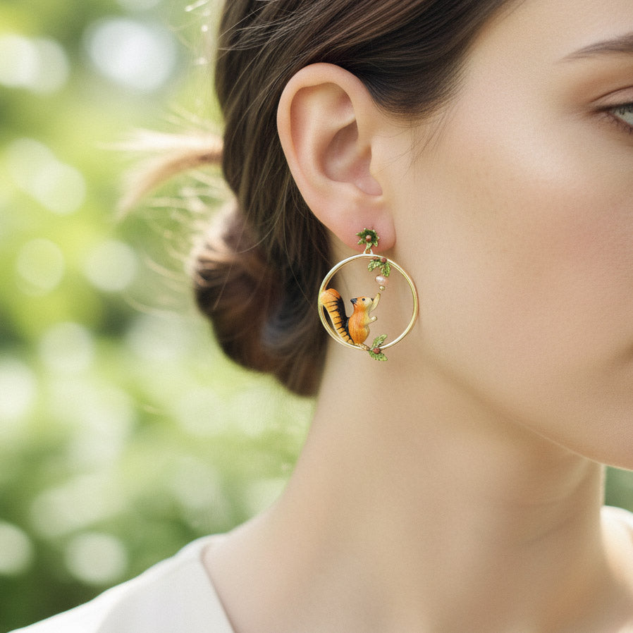 Close-up of a person wearing a gold hoop earring with a squirrel design against a blurred green background