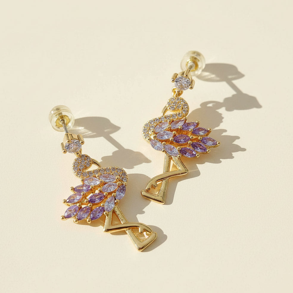 Gold flamingo earrings with purple CZ marquise stones on cream background