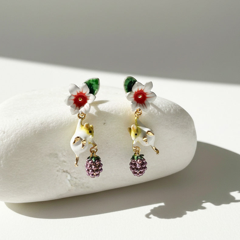 Pair of earrings with floral and mouse designs on a white stone surface