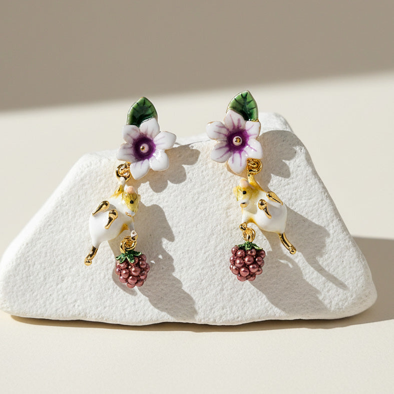 Pair of earrings with mouse, floral and berry designs on a white stone surface