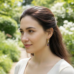 Woman with long brown hair wearing earrings in a garden setting