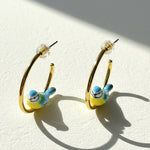 Gold hoop earrings with bird charms on a light background