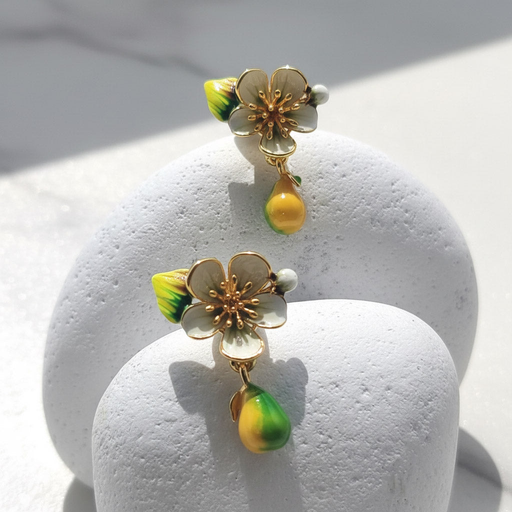 Floral earrings with gold accents and green and yellow drops on a white stand.