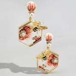 Pair of earrings with floral and bee design on a light gray background