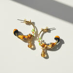 Pair of gold hoop earrings with animal-themed charms on a light background