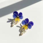 Pair of floral earrings with blue and yellow flowers and pearl-like beads on a white background