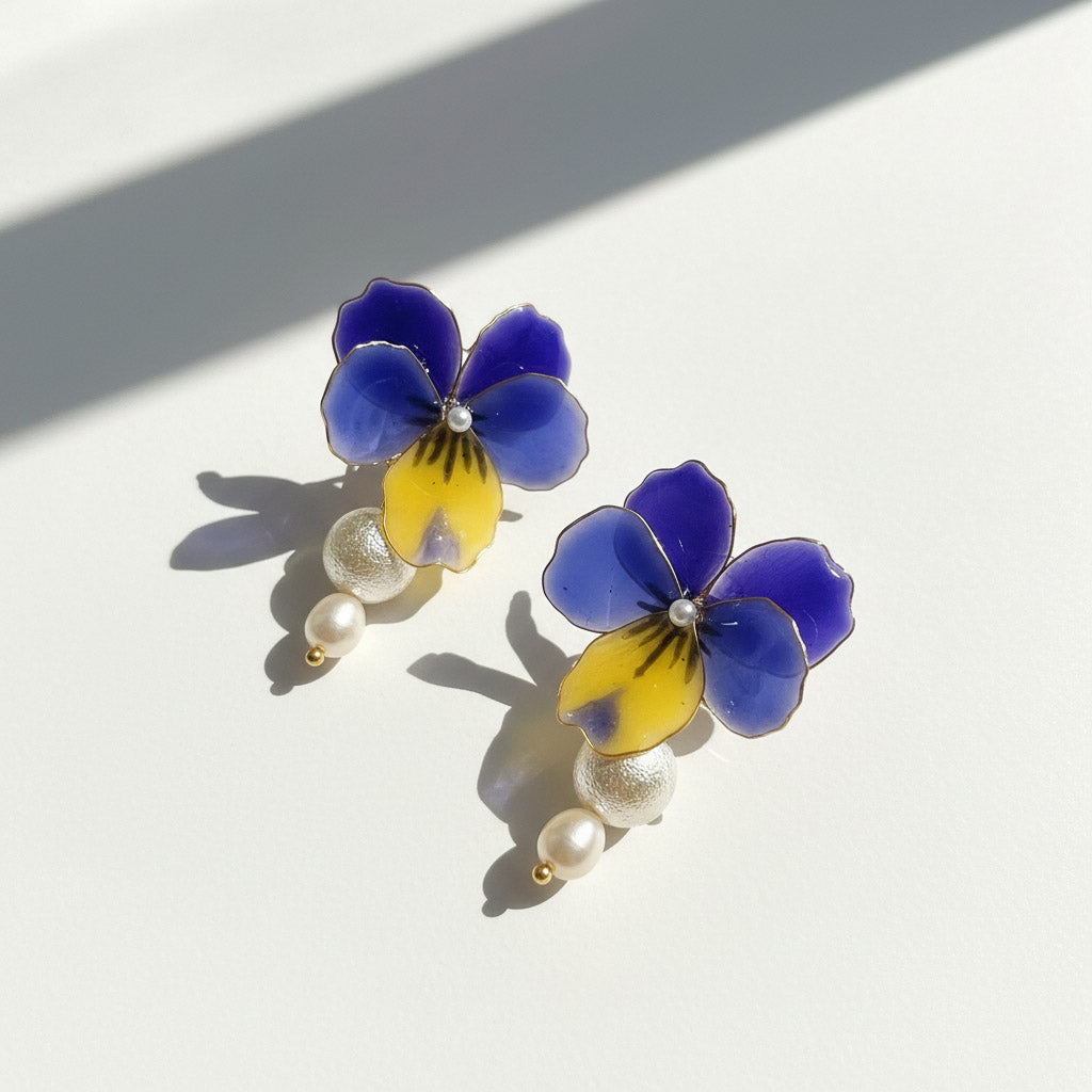 Pair of floral earrings with blue and yellow flowers and pearl-like beads on a white background