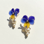 Flower-shaped earrings with blue and yellow petals and pearl-like beads on a light background