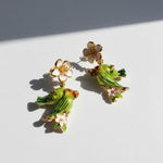 Gold earrings with hand-painted green parrots and pink enamel flowers, captured in bright natural light