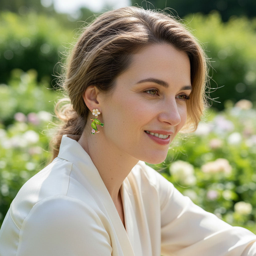 Model wearing hand-painted green parrot earrings with pink enamel flowers, photographed outdoors in sunlight