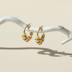 Pair of gold hoop earrings with floral designs on a white branch against a beige background