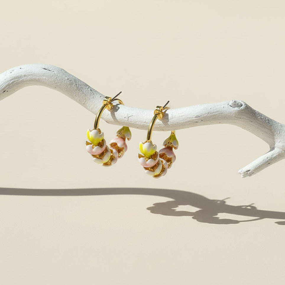 Pair of gold hoop earrings with floral designs on a white branch against a beige background