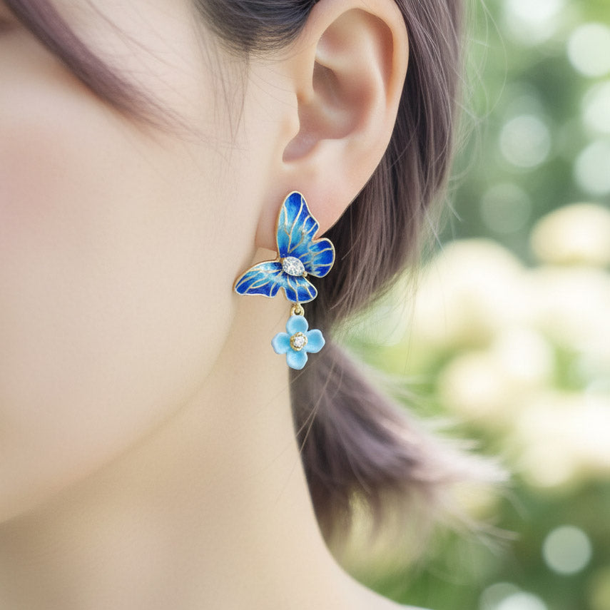 Blue butterfly earrings worn by a person with a blurred natural background