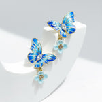 Blue butterfly earrings with flowers on a white stand