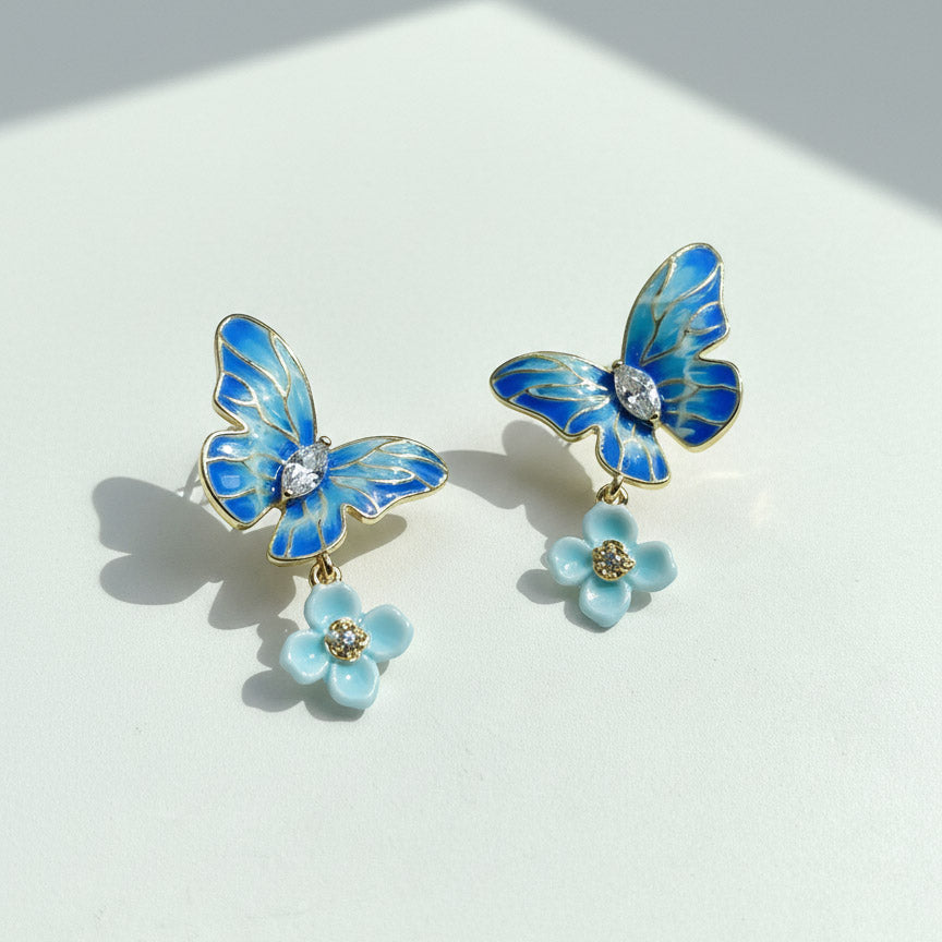 Blue butterfly earrings with flower details on a white background