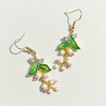 Gold earrings with green leaves and pink flowers on a light background