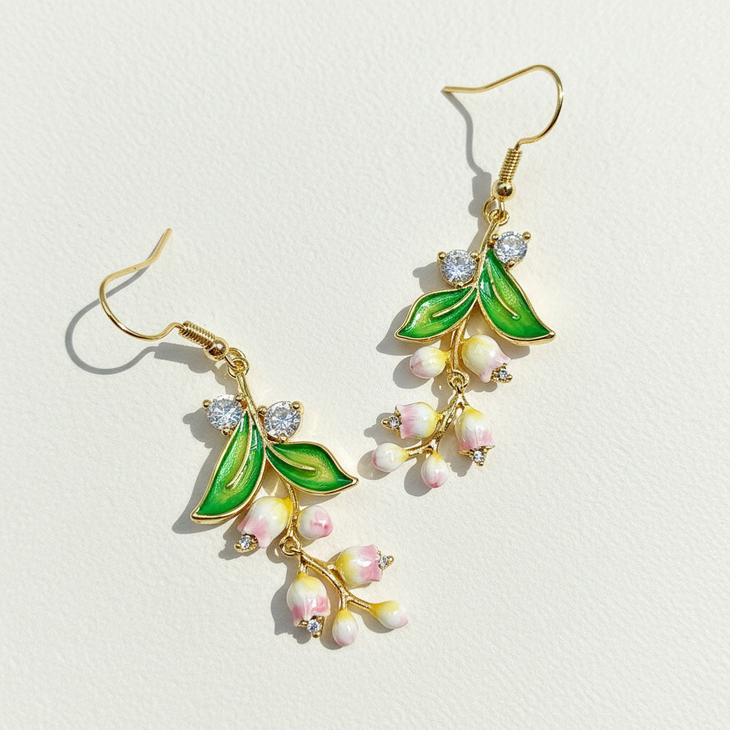 Gold earrings with green leaves and pink flowers on a light background