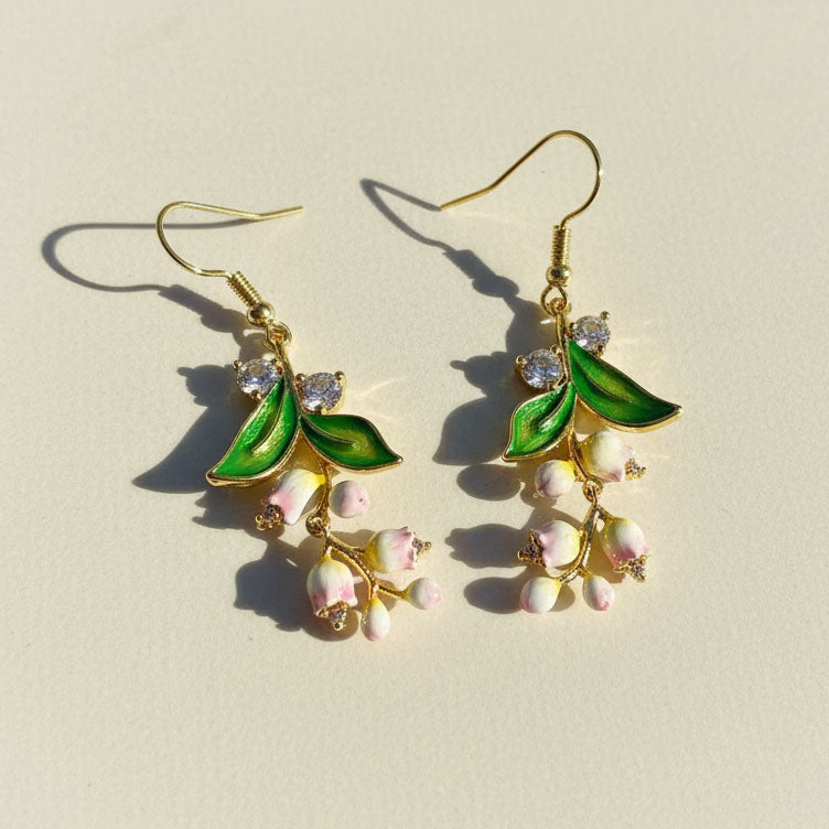 Gold earrings with green leaves and pink flowers on a beige background
