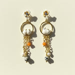 Pair of earrings with floral tops, bird-like figures, and hanging beads on a beige background