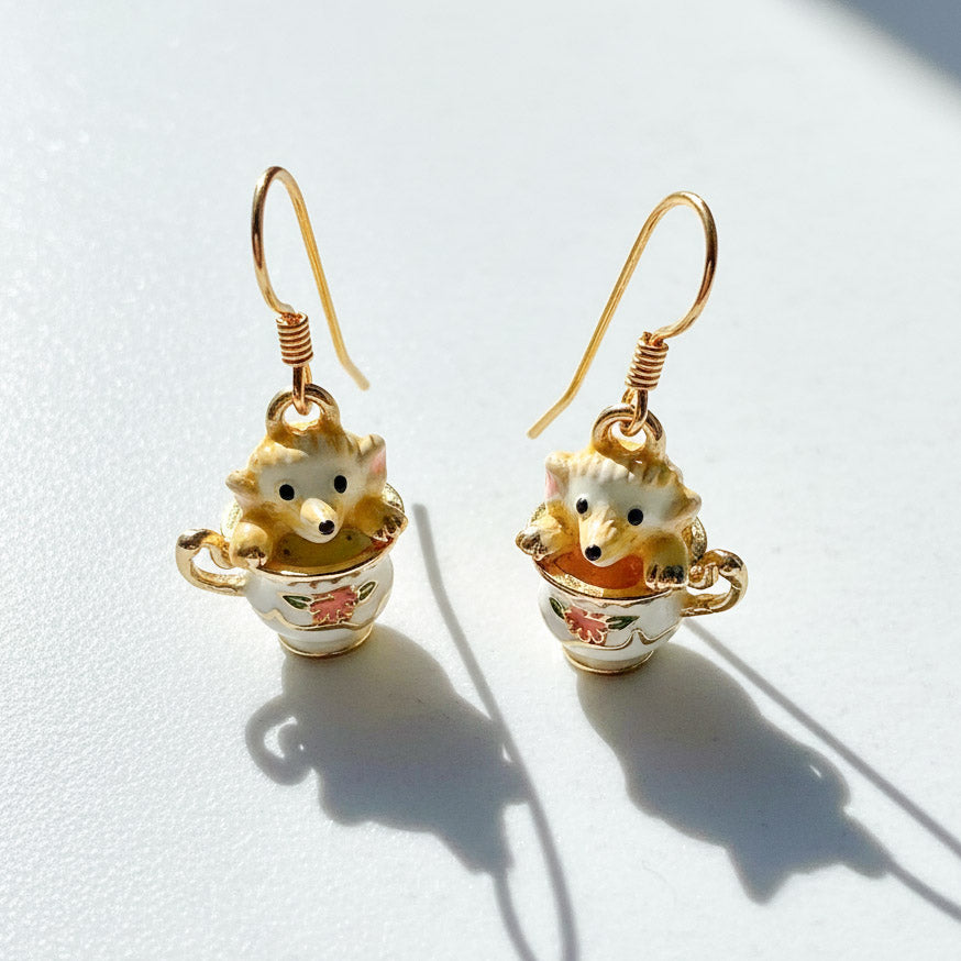 Pair of earrings with hedgehog design in a teacup on a white background
