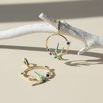 Gold earrings with bird designs on a beige surface