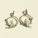 Gold hoop earrings with colorful bird and flower designs on a beige background