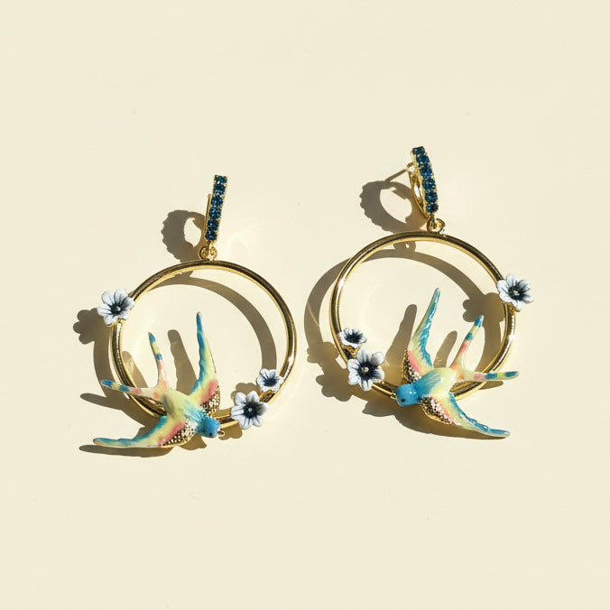 Gold hoop earrings with colorful bird and flower designs on a beige background
