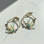 Pair of gold hoop earrings with colorful sparrow designs on a light background