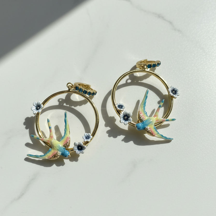 Pair of gold hoop earrings with colorful sparrow designs on a light background