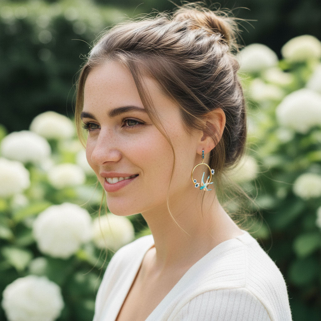 Woman wearing hoop earrings with a blurred background of white flowers and greenery