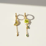 Pair of gold earrings with lemon and flower designs on a light background