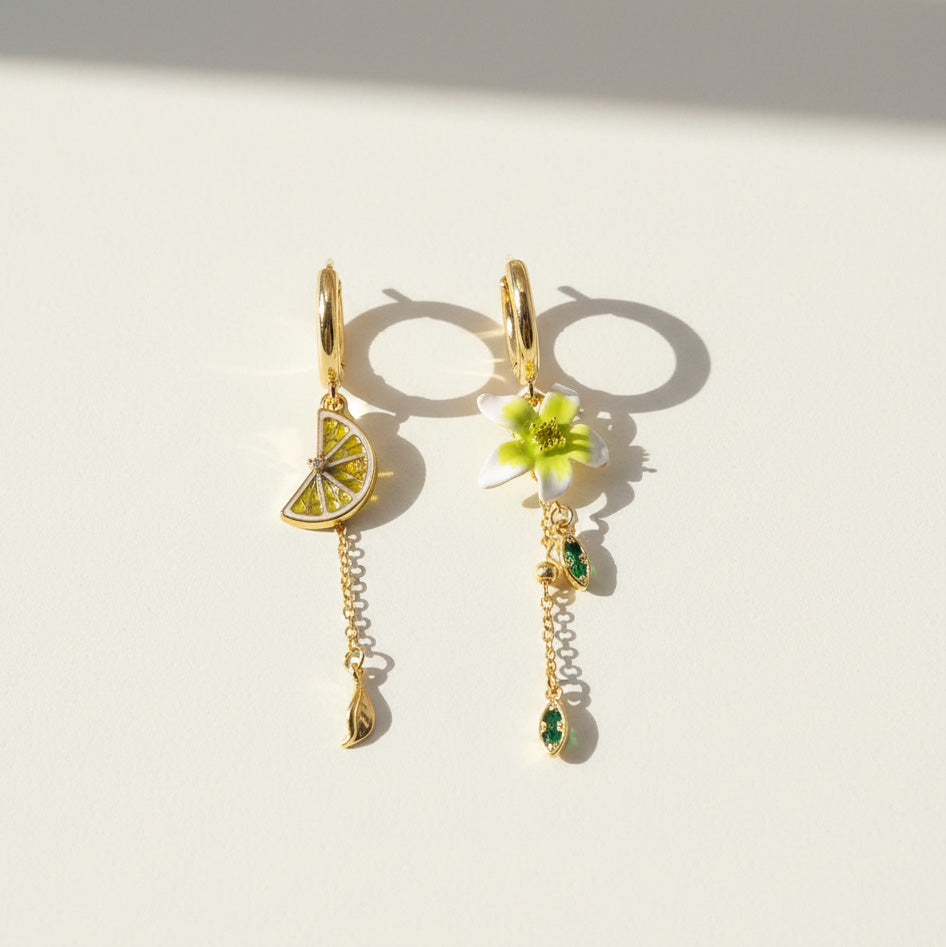 Pair of gold earrings with lemon and flower designs on a light background