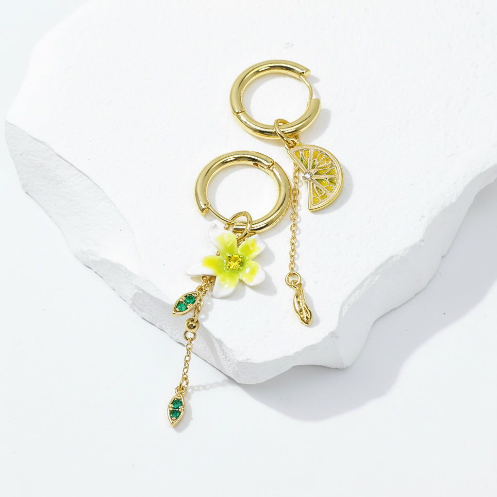 Gold hoop earrings with floral and fruit charms on a white ribbon background