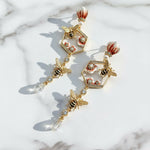 Elegant earrings with bee and floral design on a marble surface