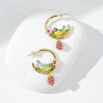 Pair of gold hoop earrings with bird and berry designs on a white background