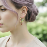 Close-up of a woman wearing gold hoop earrings with colorful charms against a blurred green background