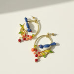 Colorful hoop earrings with bird and leaf designs on a light background