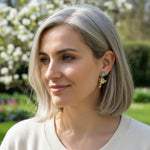 Model wearing gold frog earrings with turquoise flower studs outdoors.