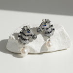 Pair of ornate earrings with pearls on a textured white surface