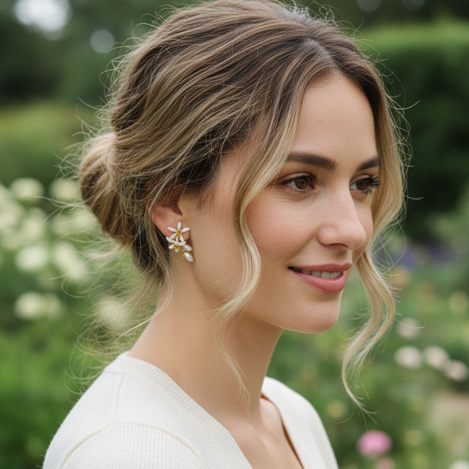 Model wearing white enamel flower and pearl drop earrings in garden.