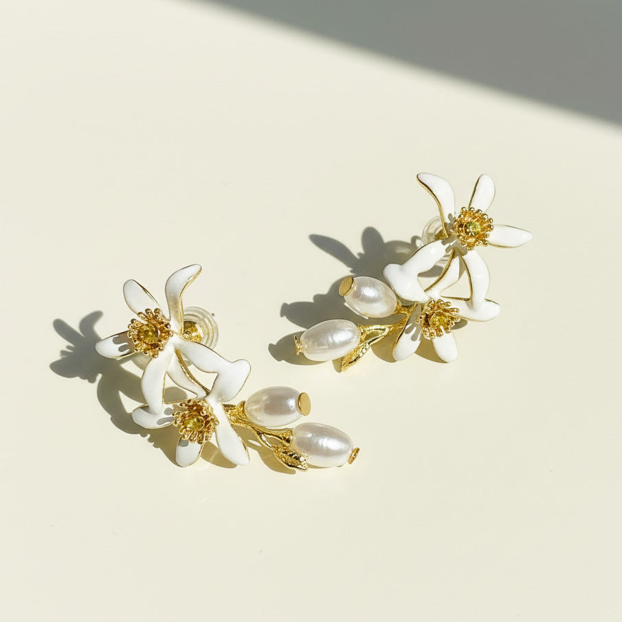 White enamel flower earrings with pearl drops on cream background.