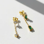Gold earrings with green and clear gemstones on a white background