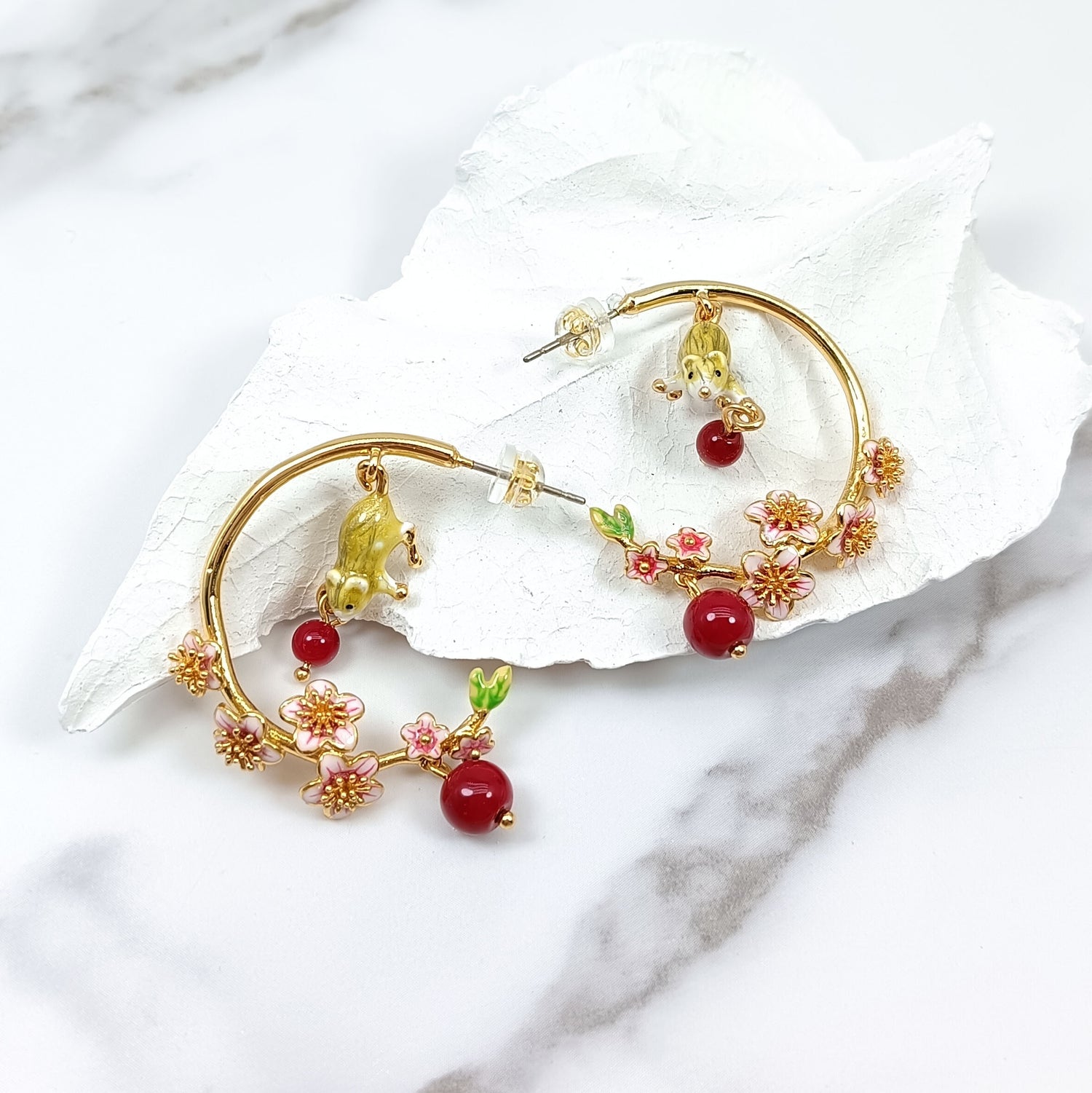 Gold-plated hoop earrings with hand-painted mouse charms and red floral enamel details, elegantly displayed on white textured background