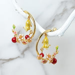 Gold-plated hoop earrings featuring hand-painted mouse charms and red floral enamel accents, displayed on a marble background.