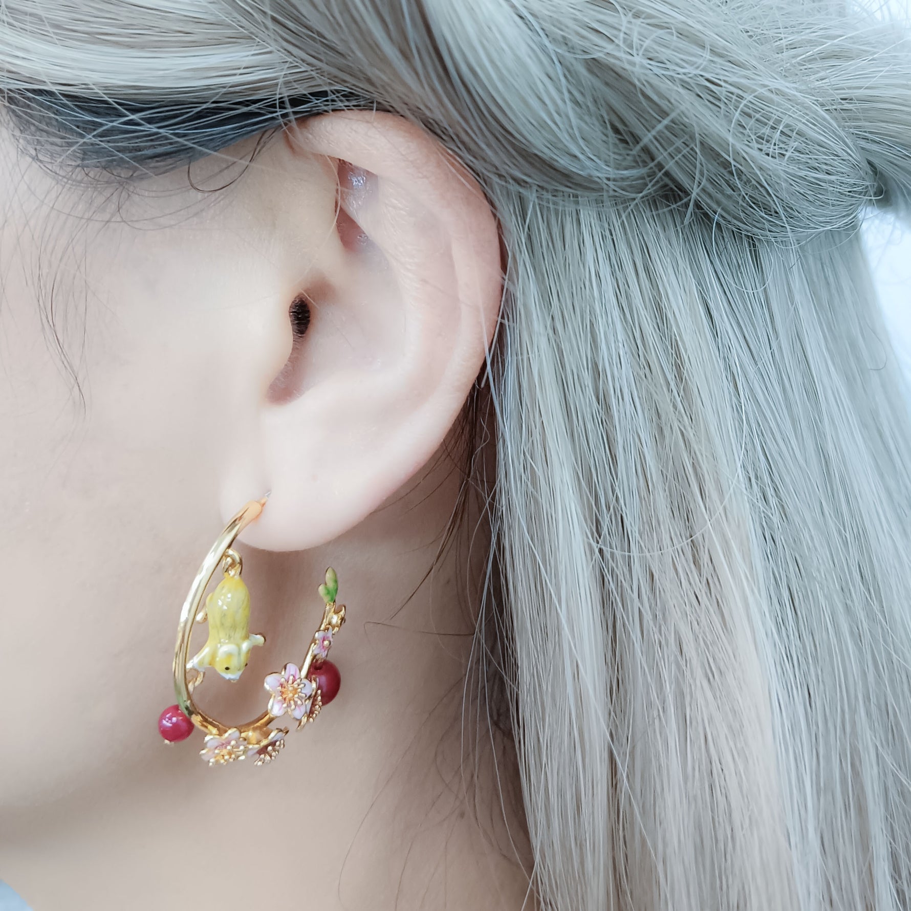 Mouse and cherry blossom hoop earrings with red bead accents, displayed on a model’s ear against a silver hair backdrop.
