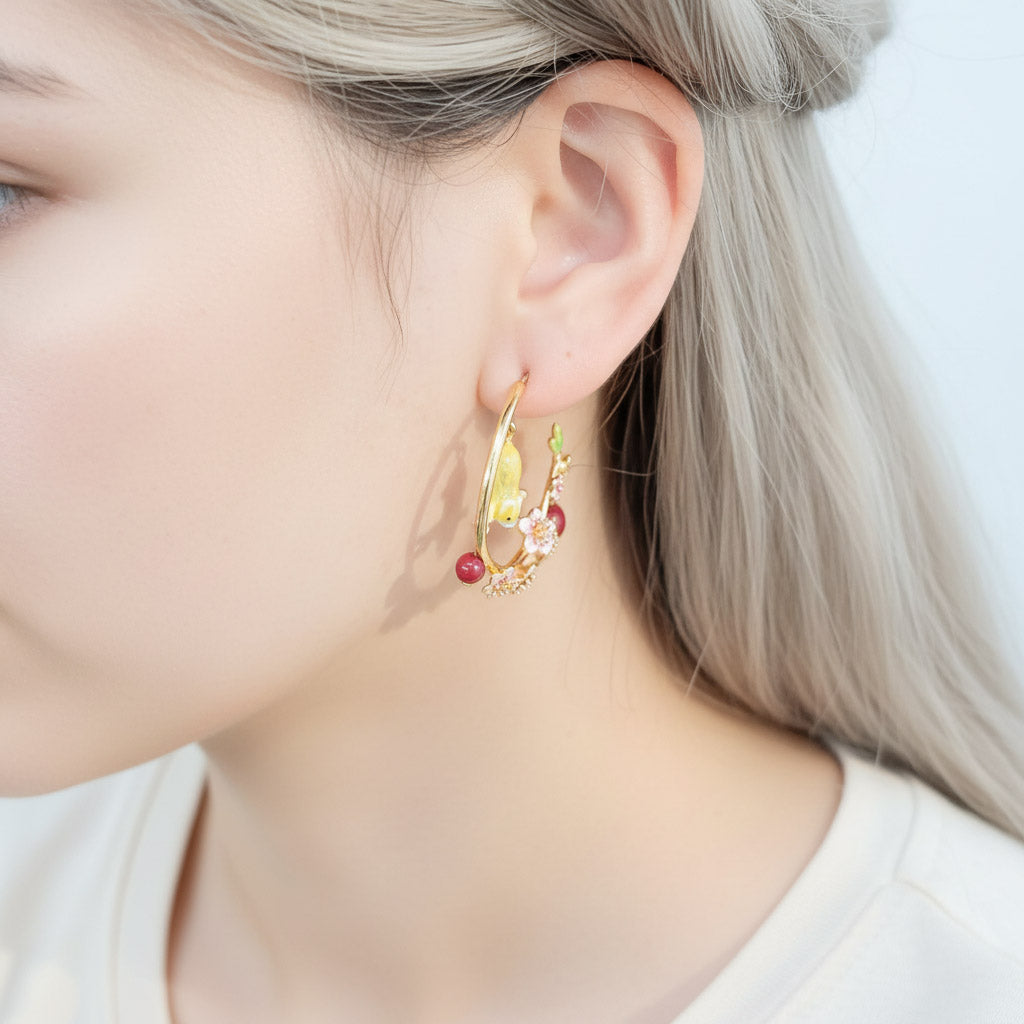 Close-up of a person wearing gold hoop earrings with red gemstones.