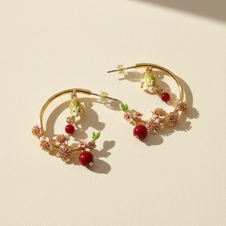 Gold hoop earrings with floral and berry designs on a beige background