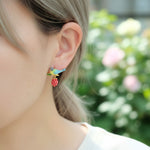 Close-up of an ear wearing a colorful bird and berry earring with a blurred floral background