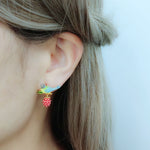 Bird and berry enamel stud earrings on a woman’s ear, hair pulled back for display.
